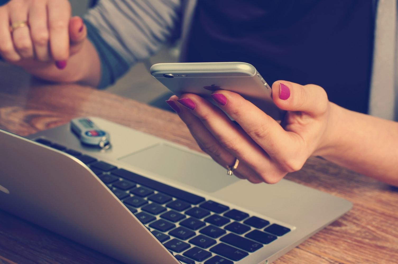 woman holding phone next to laptop