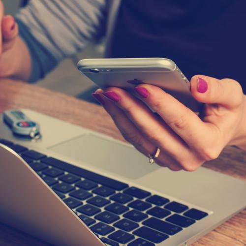 woman holding phone next to laptop